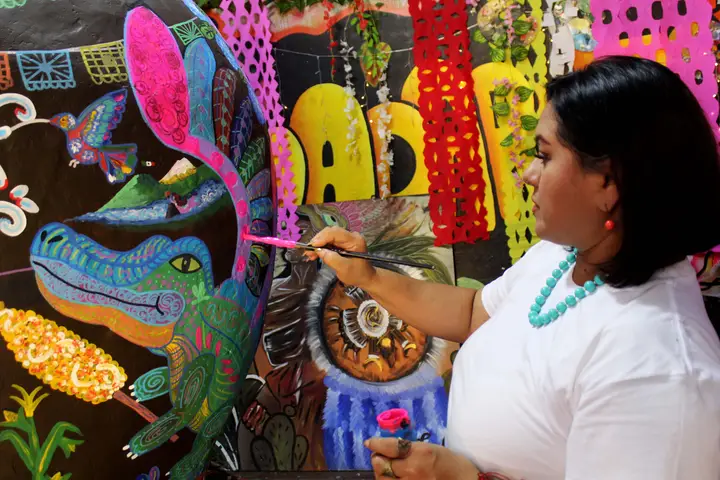 Artista de Yadarte pinta una iguana entre hojas de cempasúchil en la calavera.