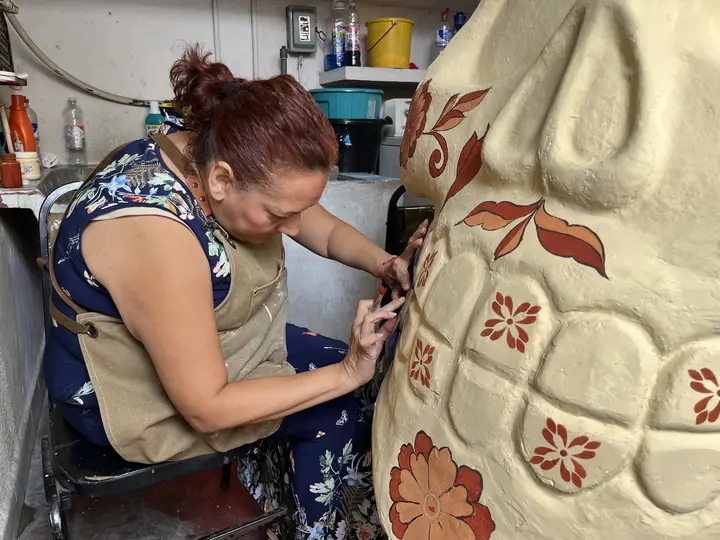 Irma Rosa Alavez Castillo pinta flores rojas sobre una calavera de tono marfil.