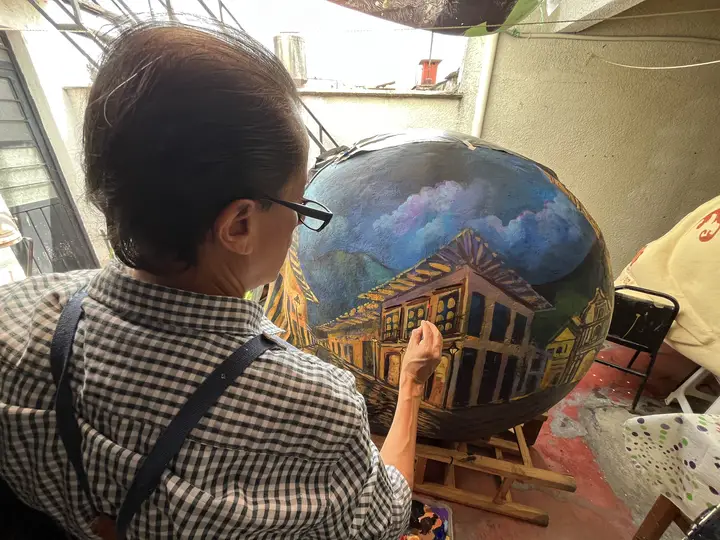 Artista aplica el trazo de un edificio sobre la calavera azul.