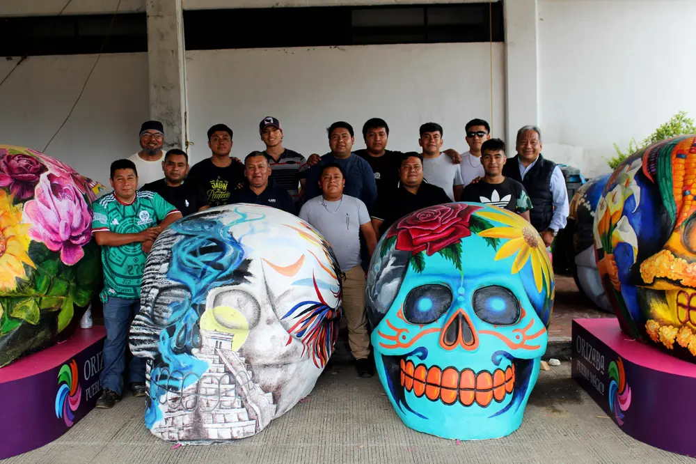 El equipo de Desfiles y Festejos posa con las calaveras monumentales en el taller.