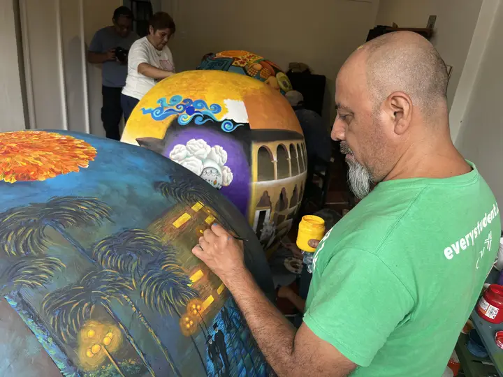 Artista de camiseta verde aplica pinceladas largas sobre la calavera.